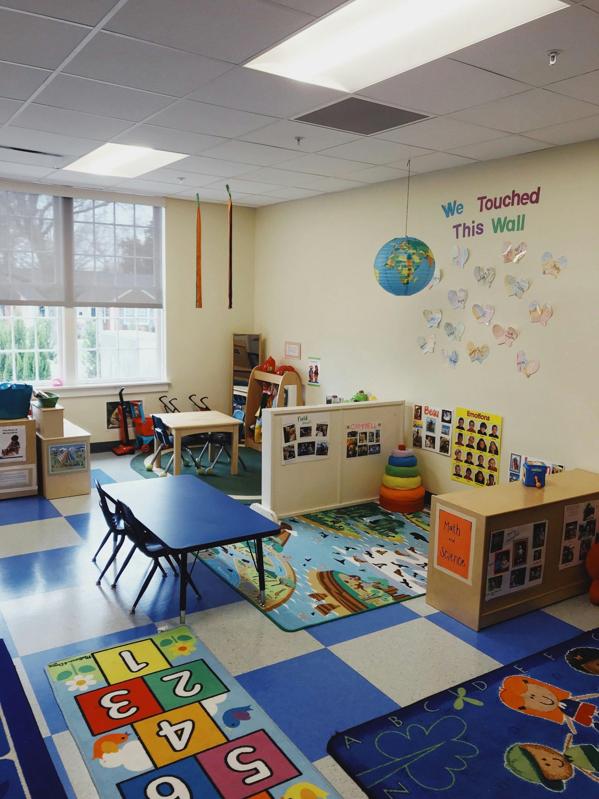 A classroom with small tables, chairs, and colorful rugs