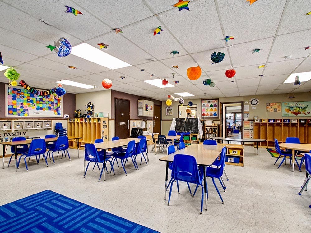 An empty classroom with small tables and blue chairs