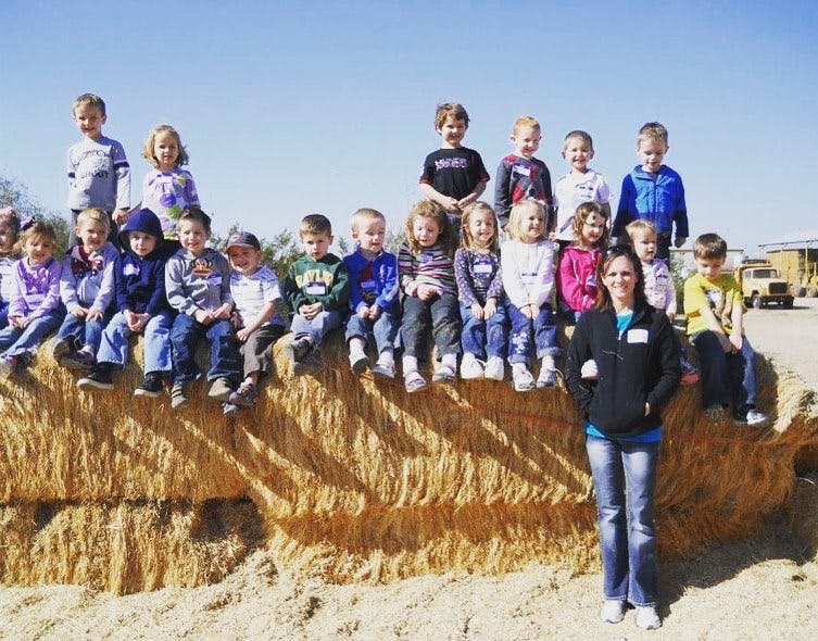 Group of children and one adult sitting and standing on hay bales