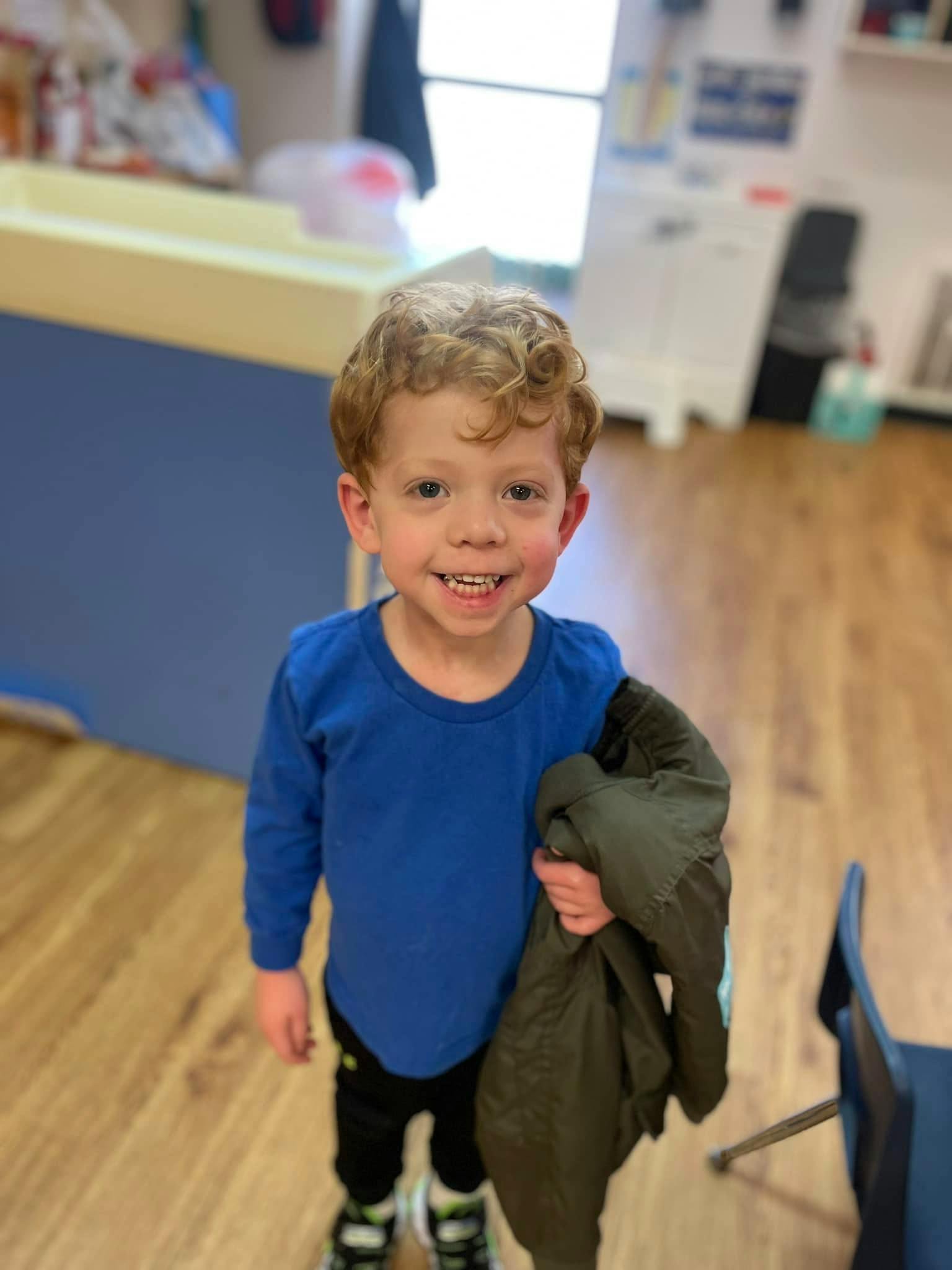 Child wearing a blue shirt holding a jacket in a classroom