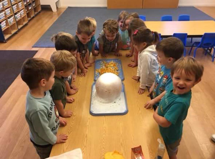 Children gathered around a table looking at a large white sphere