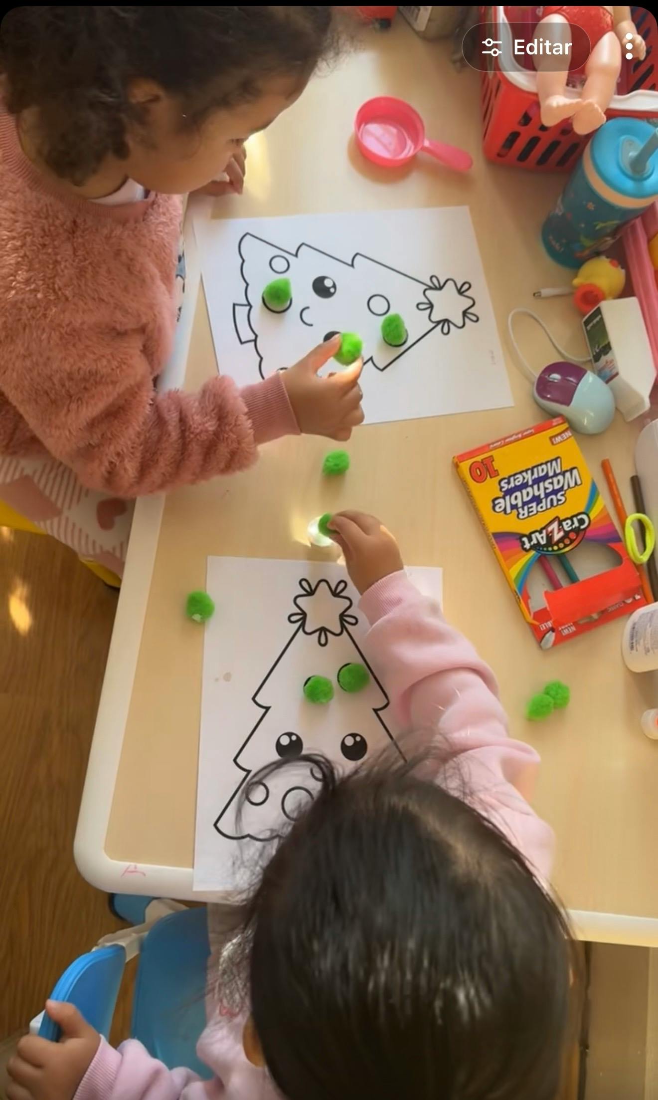 Two children decorating Christmas tree drawings with green pom-poms