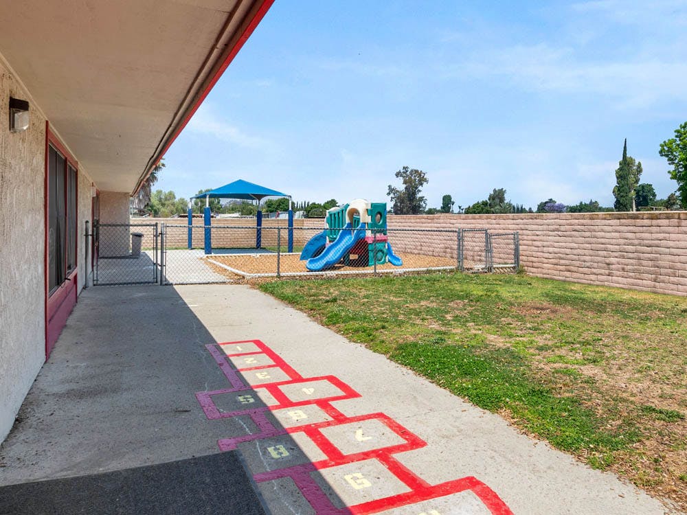 Hopscotch game on a sidewalk with a playground behind a fence