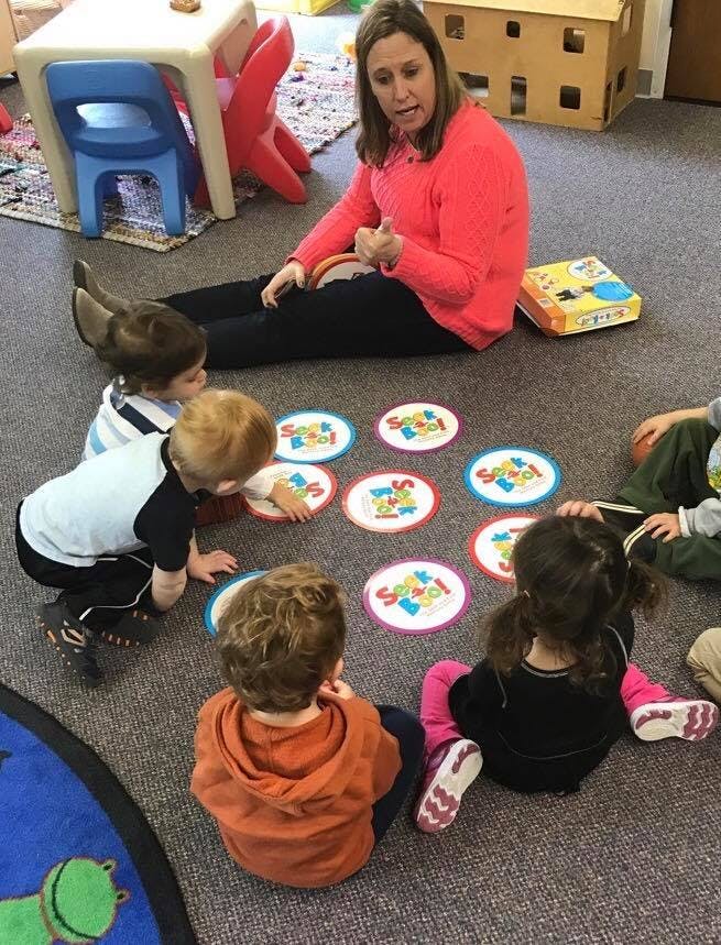 Person sitting on floor with children playing a game with colorful discs