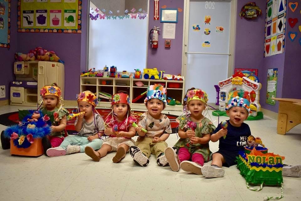 Five children wearing decorated crowns sitting on the floor in a classroom