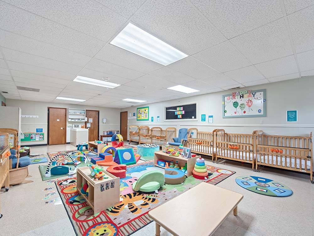 A childcare room with cribs, play mats, and soft play equipment