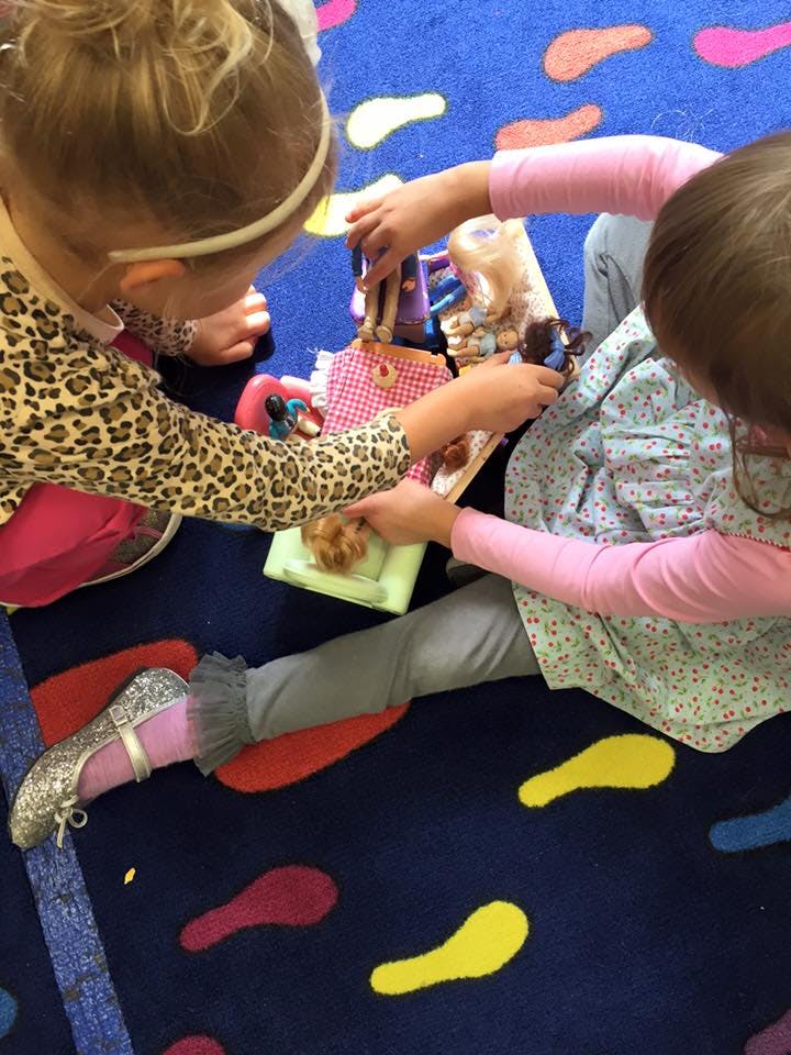 Two children playing with dolls and toy food on a colorful rug