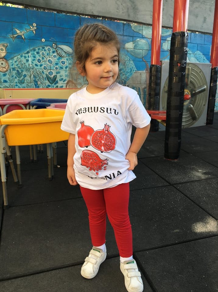 Child wearing a white t-shirt with pomegranates and red pants