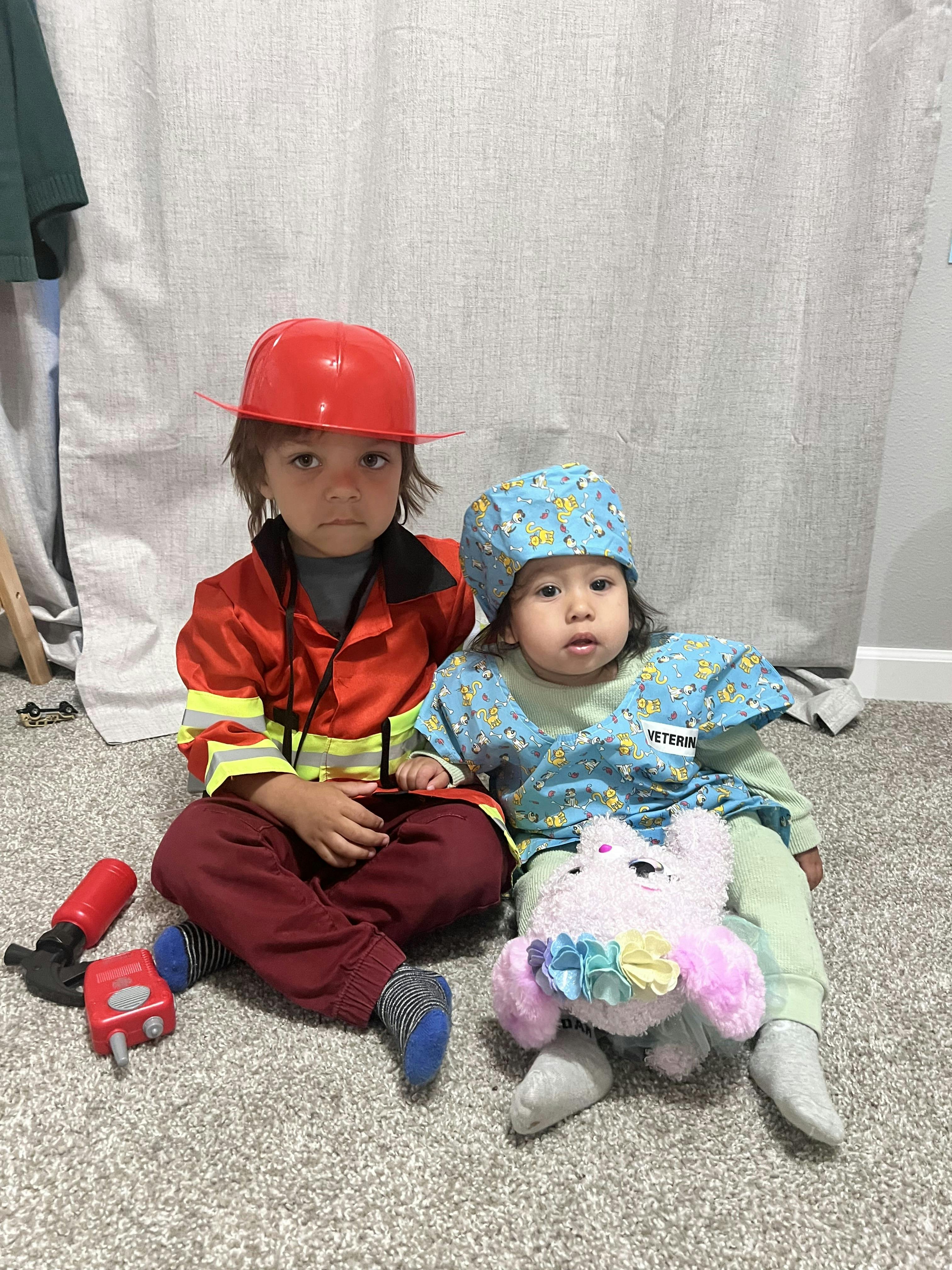 Two children in costumes, one in a firefighter costume and one in a veterinarian costume