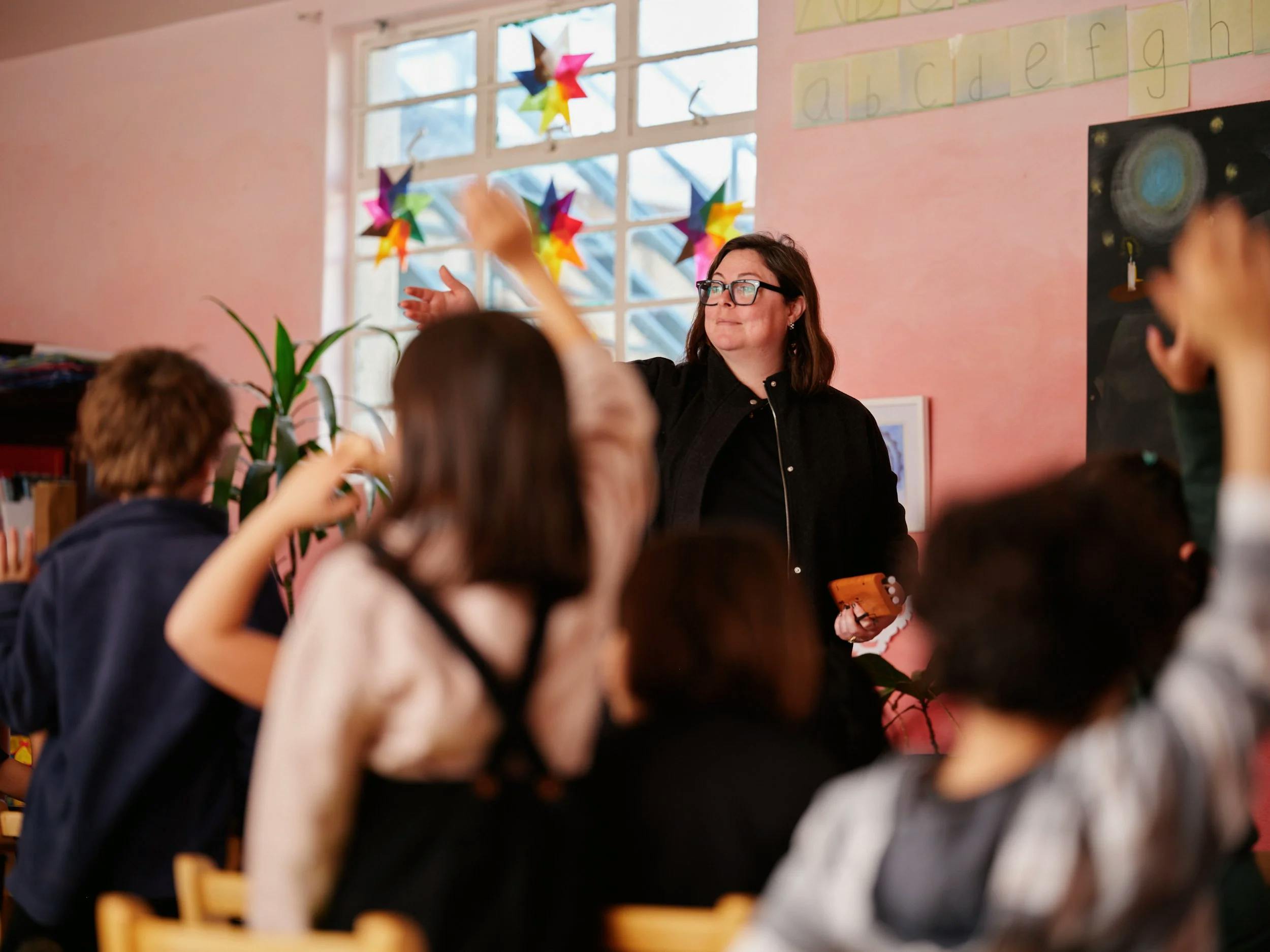 Teacher talking to a class of children with hands raised