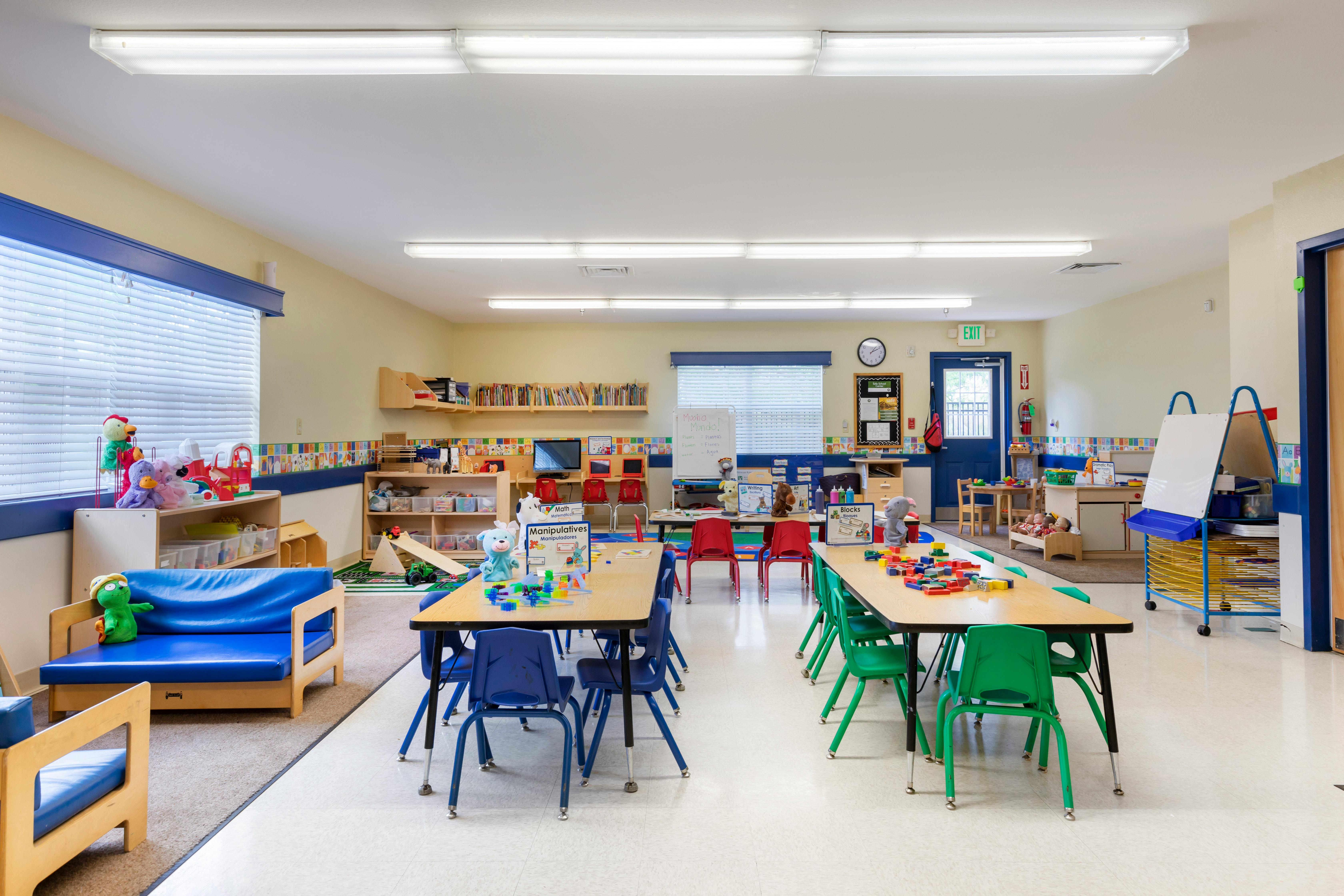 An empty children's classroom with several tables, chairs, and play areas