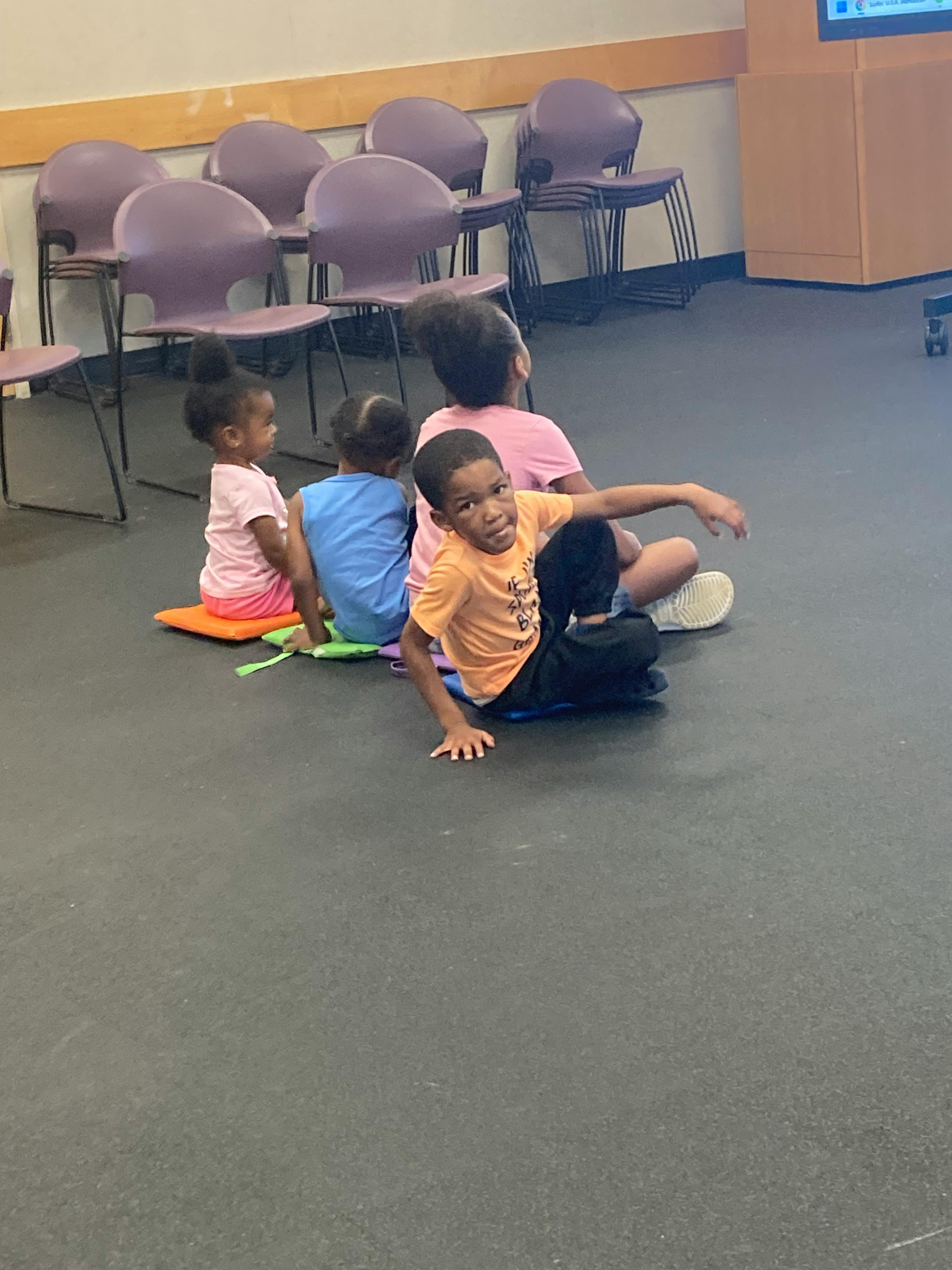 Group of children sitting on the floor in a room with chairs