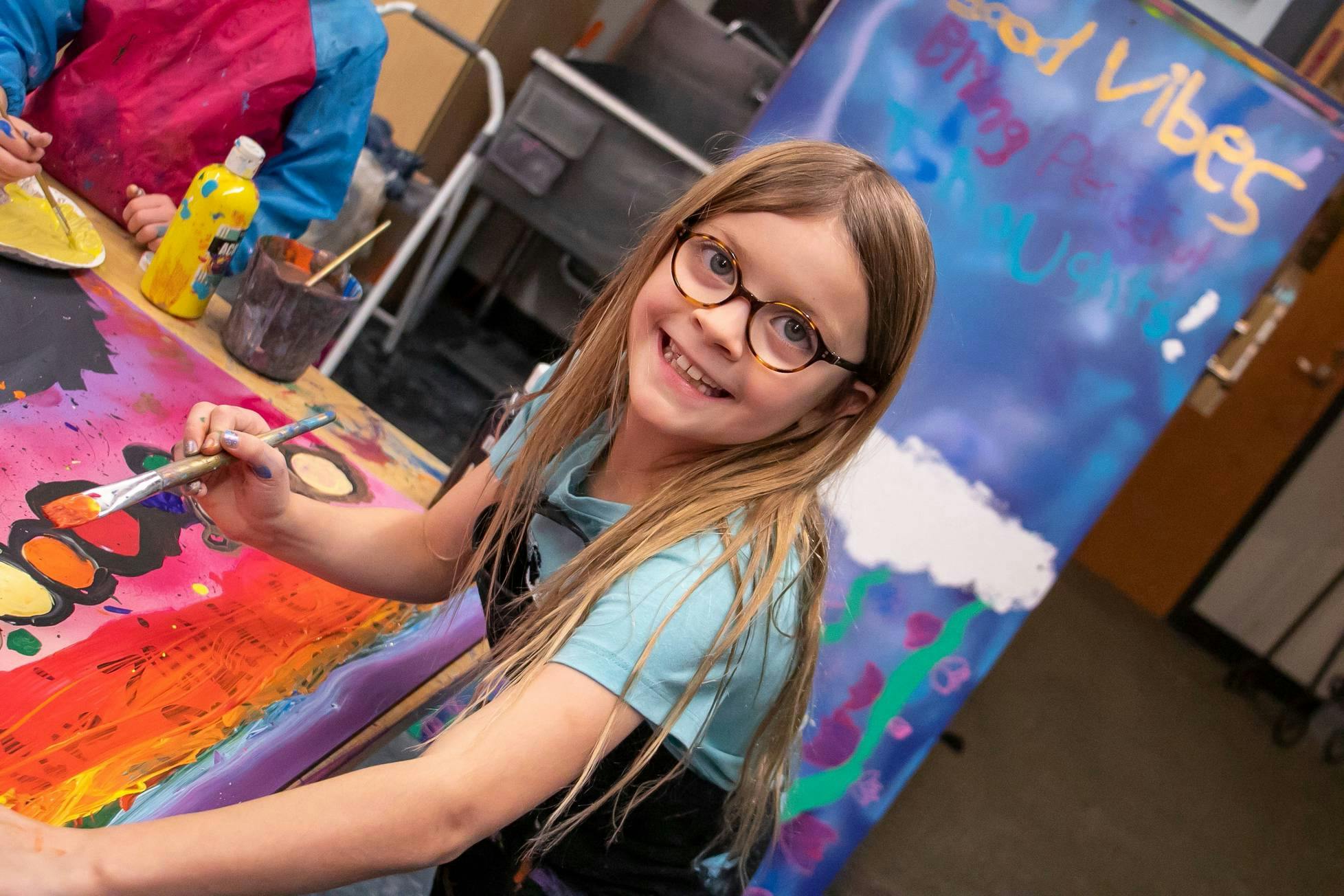 Child in glasses painting a colorful canvas