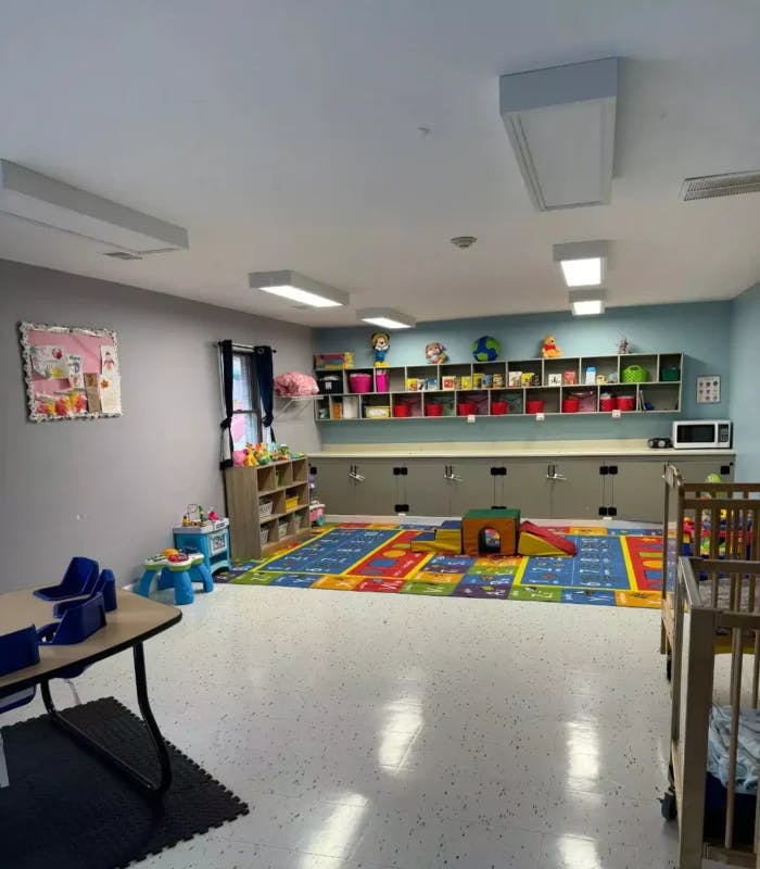 Empty daycare room with colorful rug, shelves, and cribs
