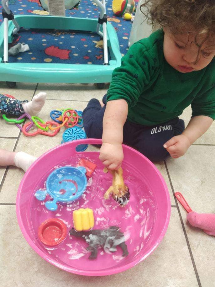 Child playing with toys in a pink basin of water