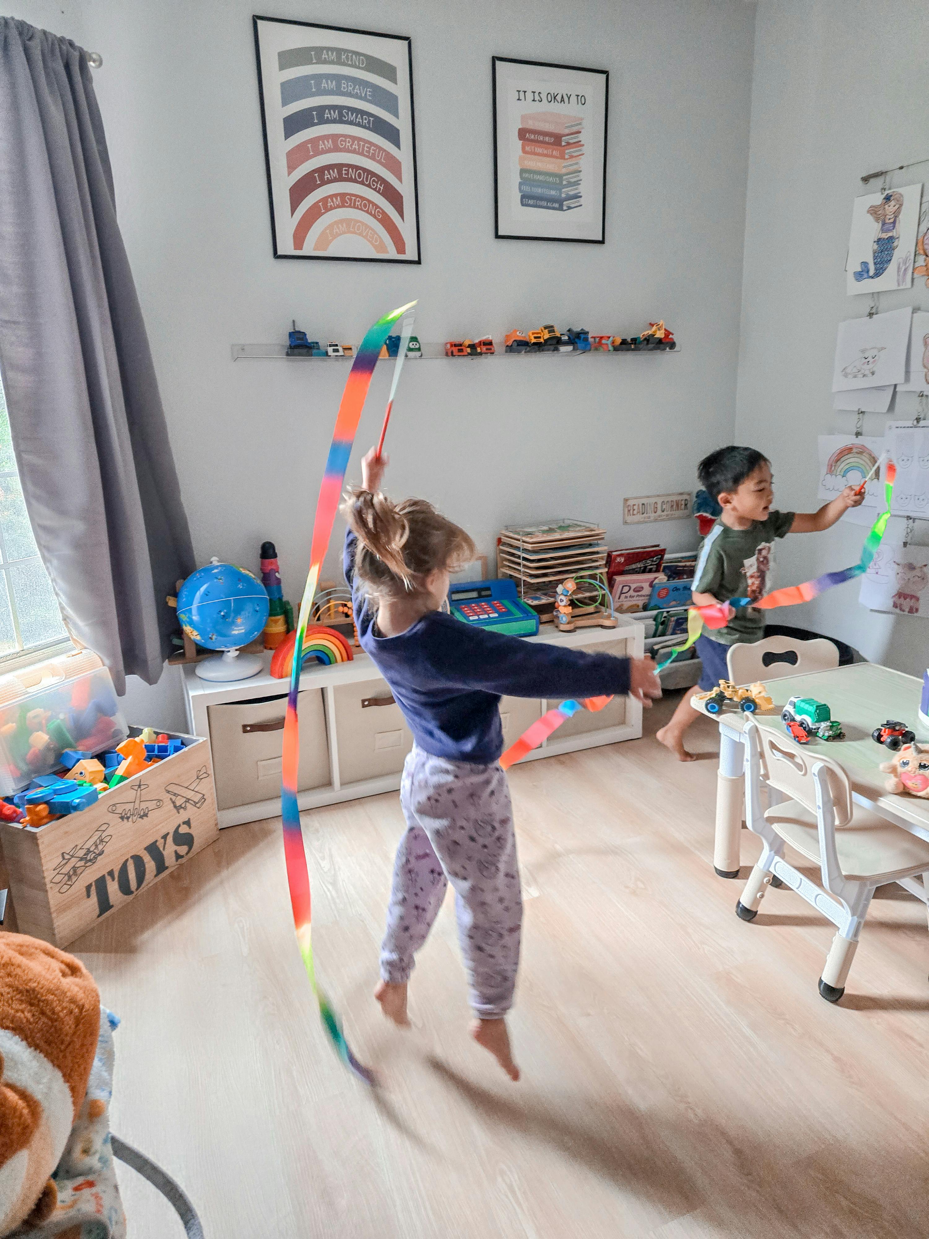 Two children playing with rainbow gymnastic ribbons in a playroom