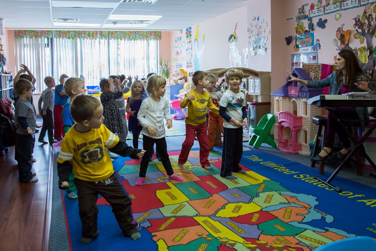 Children dancing on a map rug in a classroom with a person at a keyboard