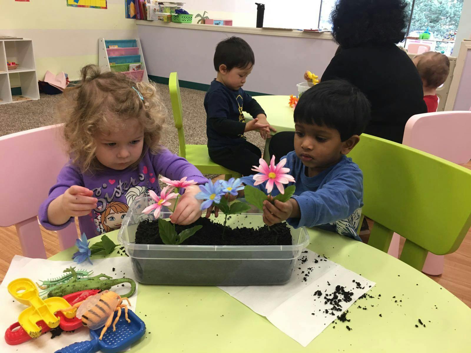 Children playing with artificial flowers and soil in a classroom