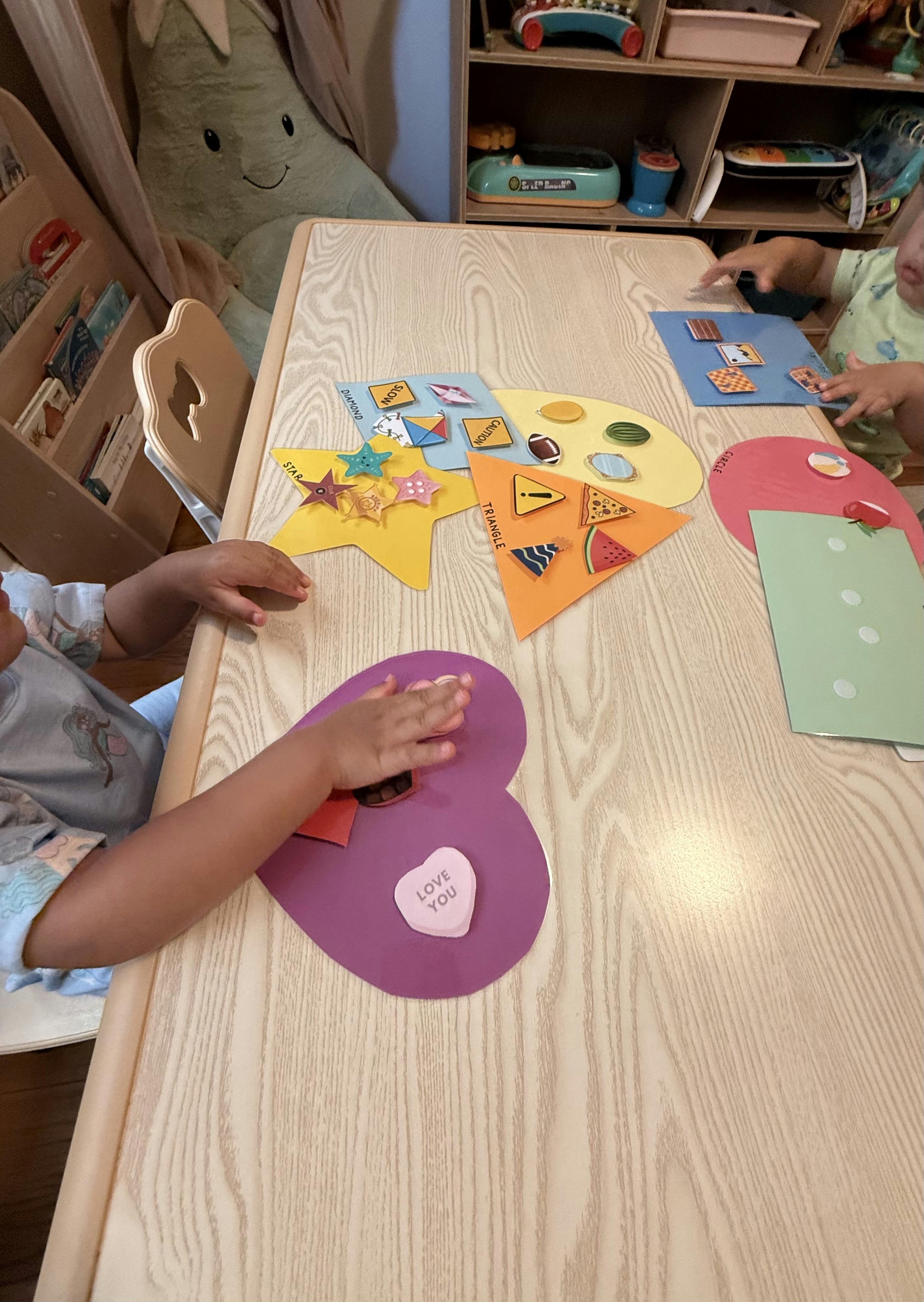Children placing shape-themed cutouts on a wooden activity table