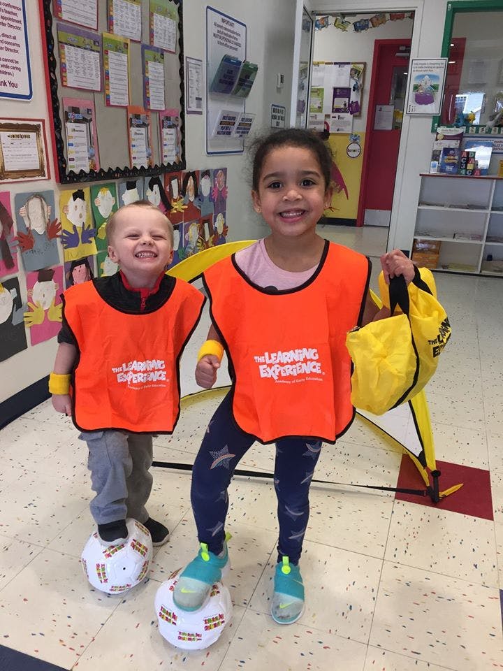 Two children in orange vests standing with soccer balls