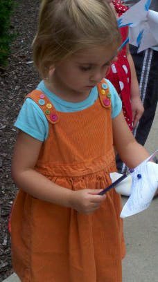 Child in an orange dress holding a paper pinwheel