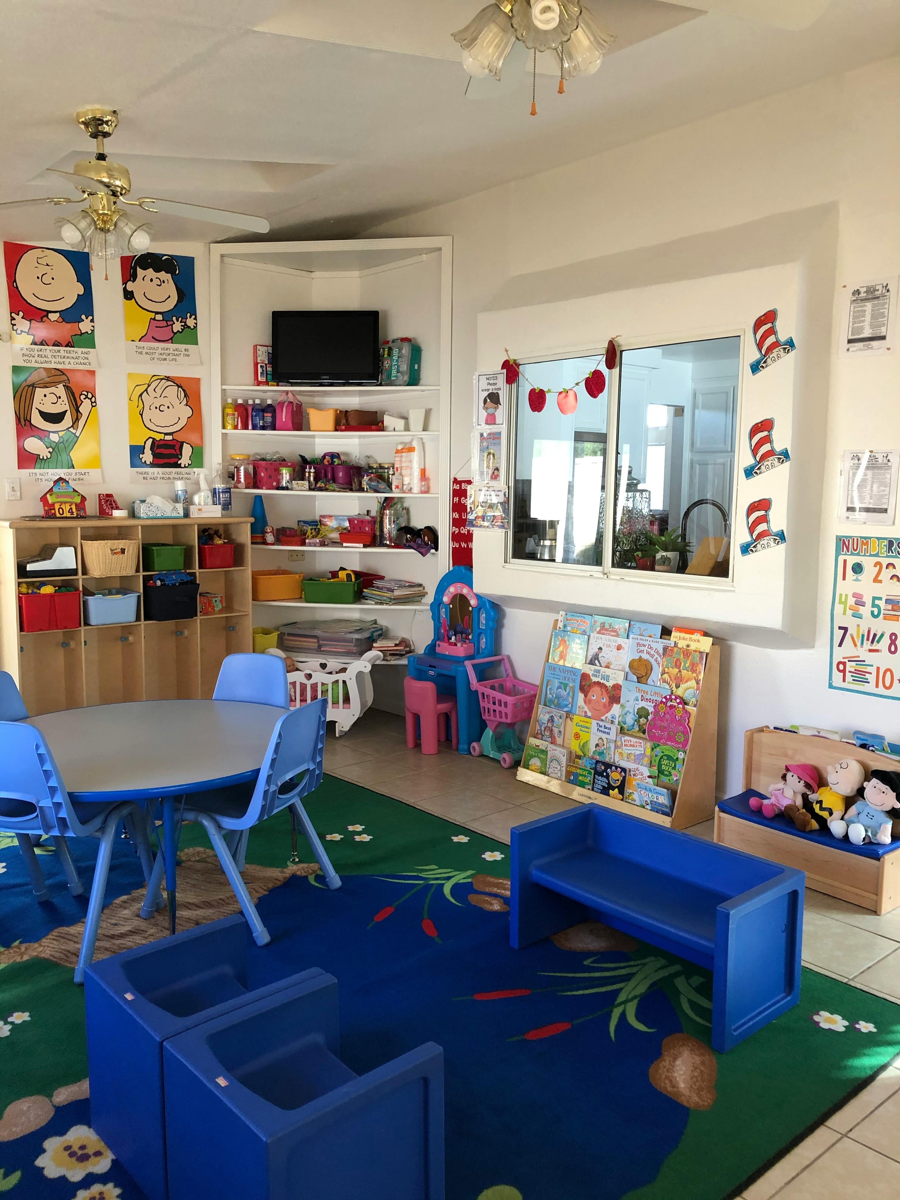 A classroom with small tables and chairs, shelves with toys, and colorful rugs