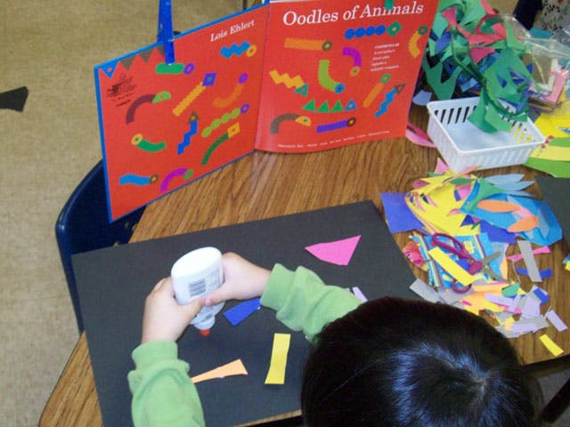 Child gluing paper shapes onto a black sheet of paper