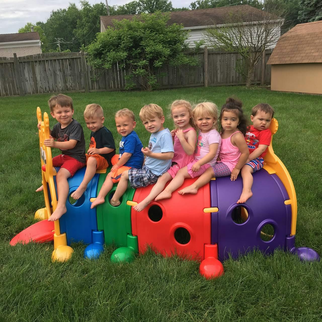 Seven children sitting on a colorful caterpillar play structure