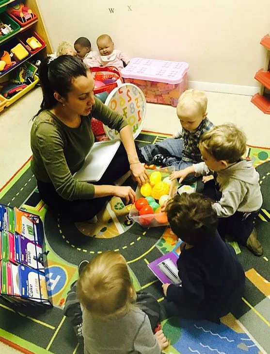 Adult and multiple children sitting on a rug playing with colorful balls