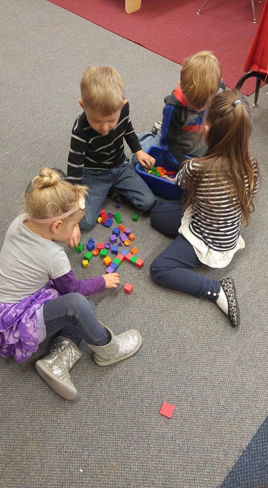 Four children playing with colorful building blocks on a carpeted floor