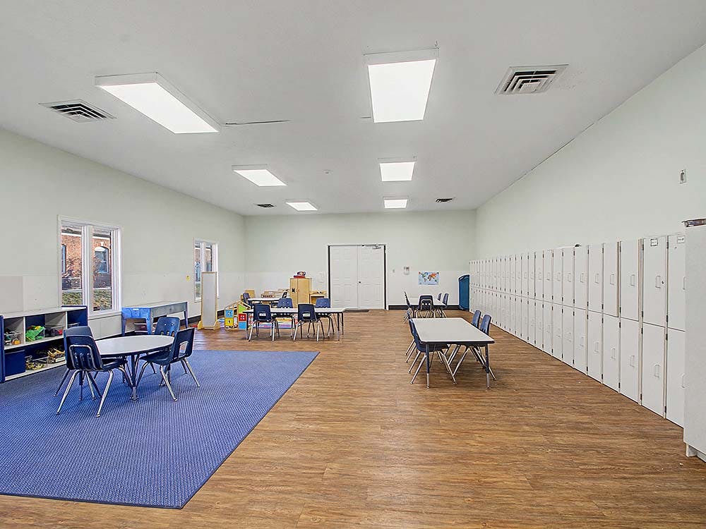 Classroom with tables, chairs, lockers, and a blue rug