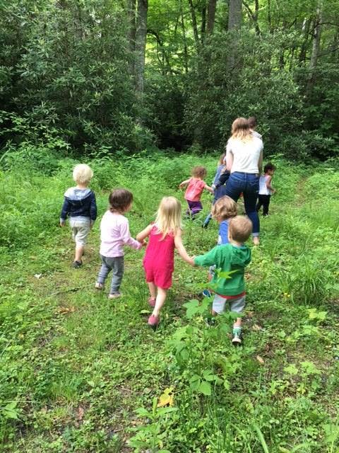 Adult and children walking through a grassy, wooded area