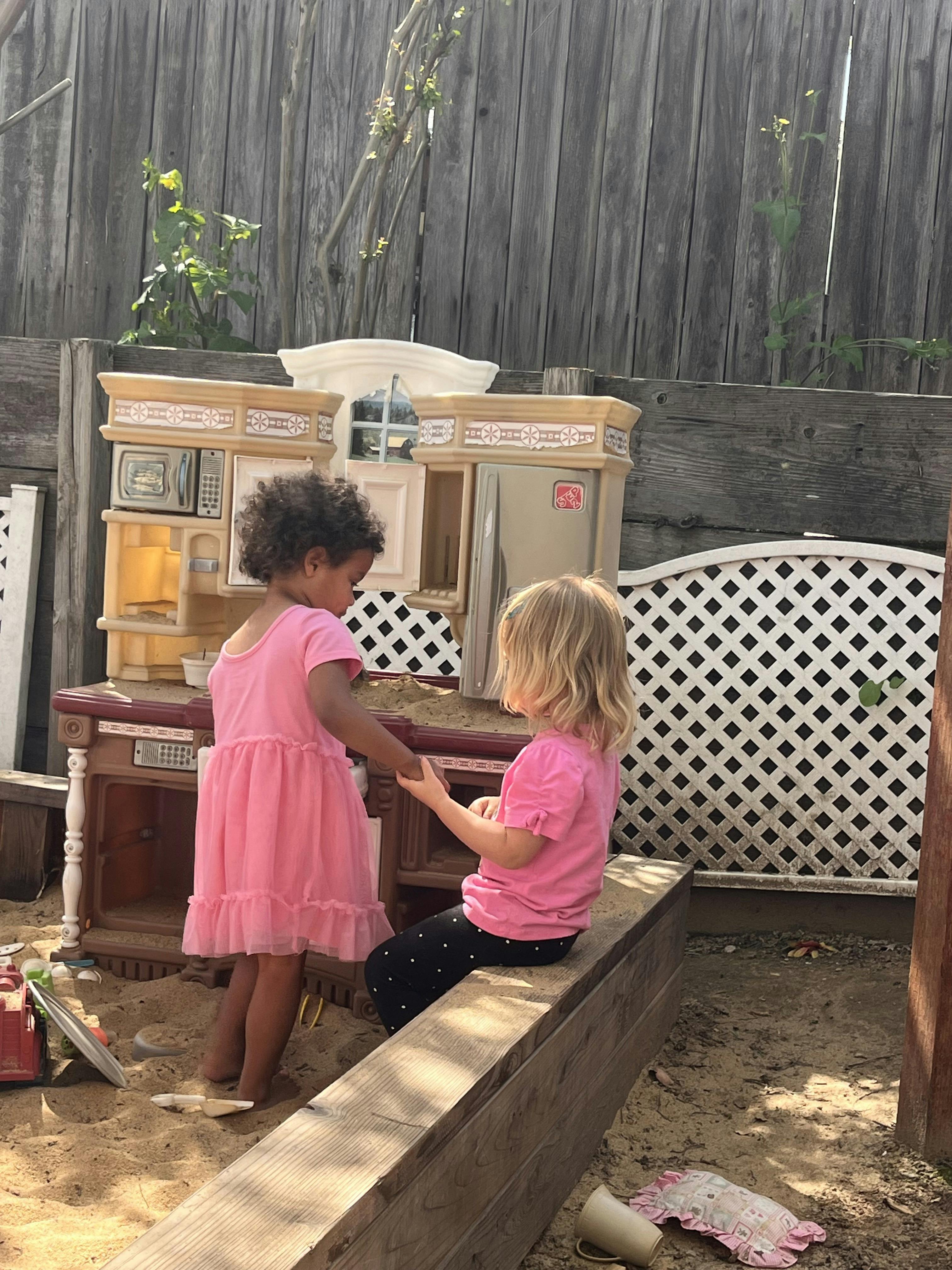 Two children playing with a toy kitchen in a sandbox