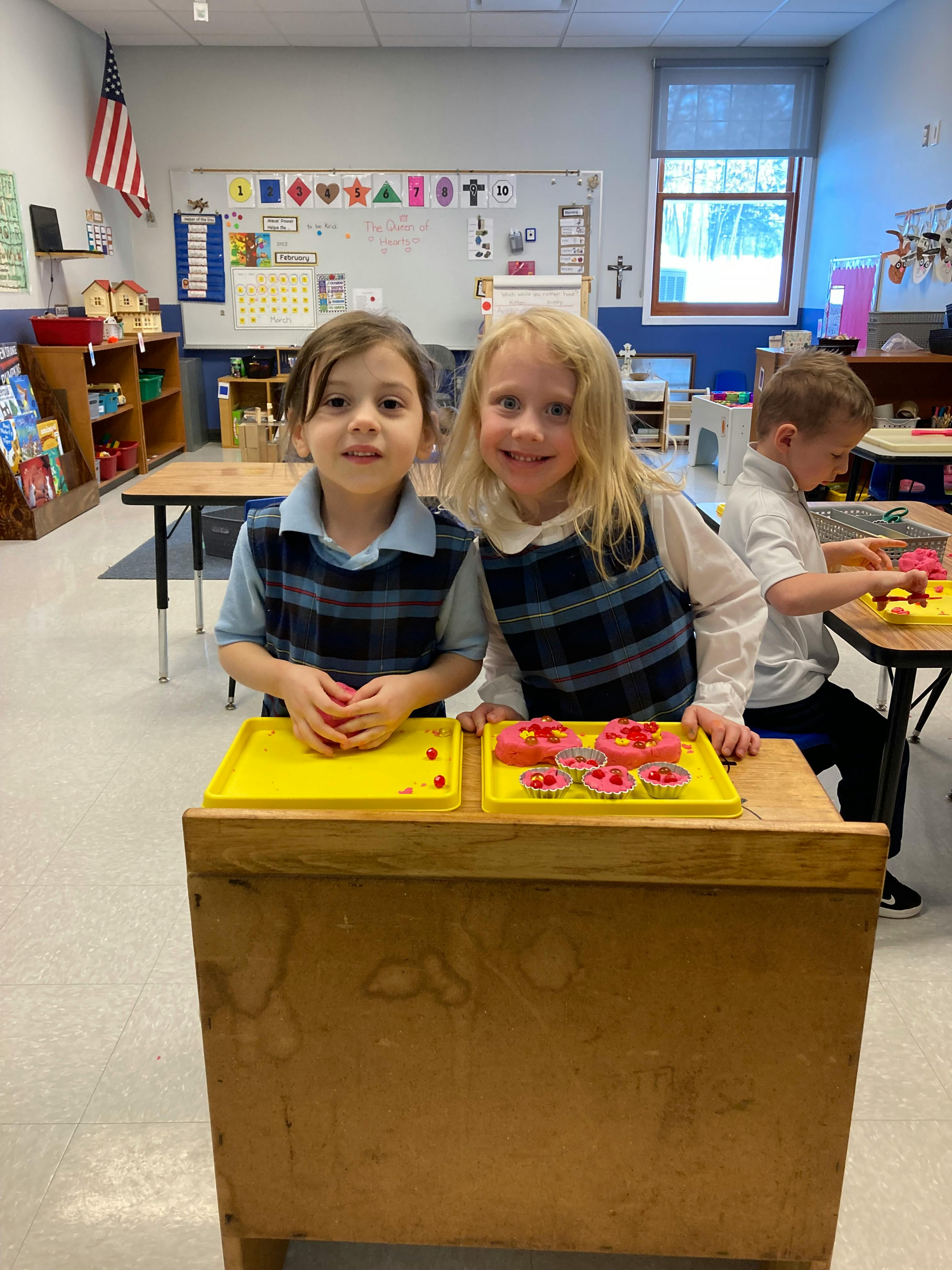 Two children standing behind trays of play food in a classroom