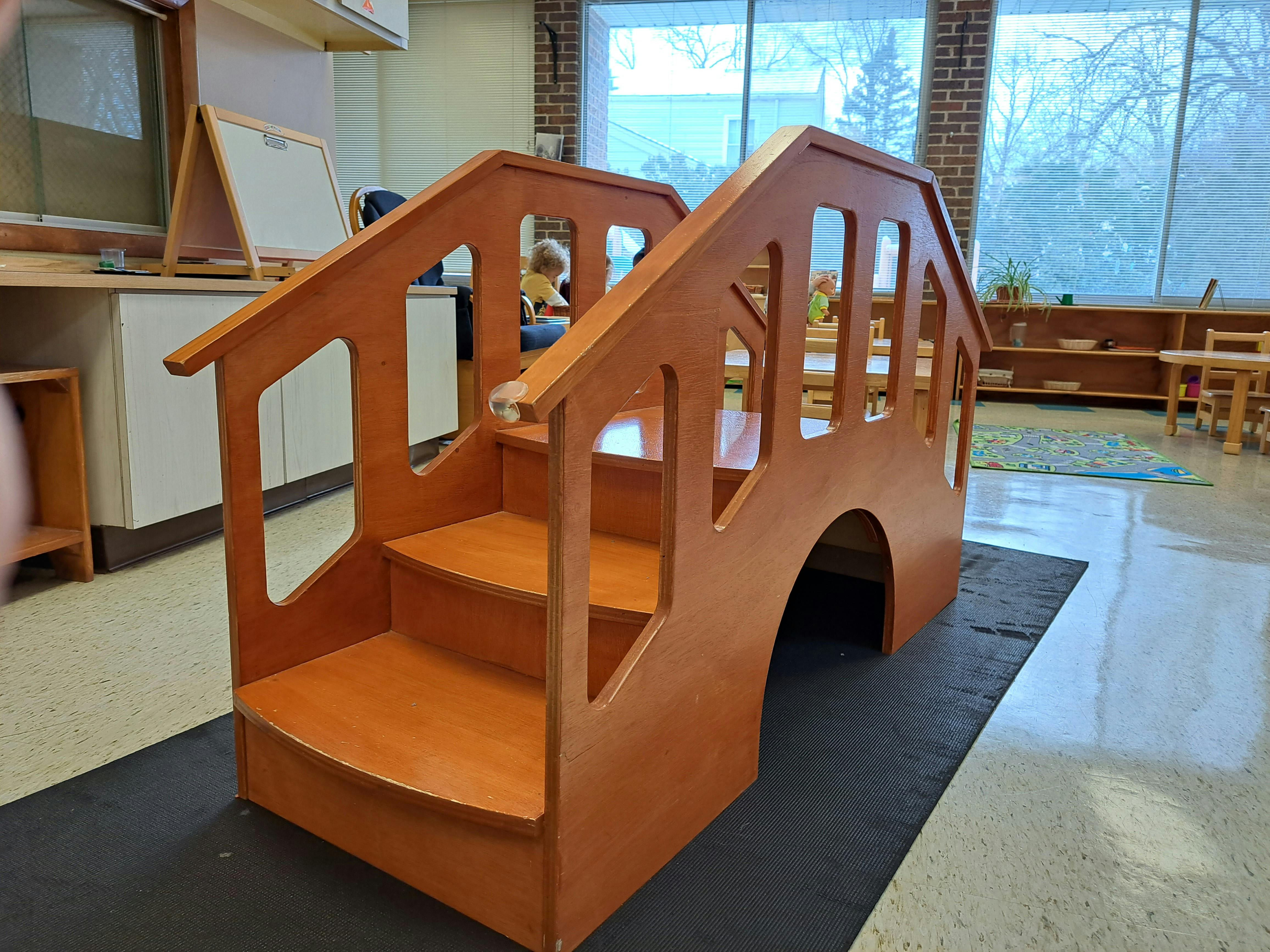 Wooden play structure with stairs and an archway in a classroom