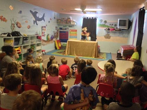 Children sitting on the floor watching a puppet show in a classroom