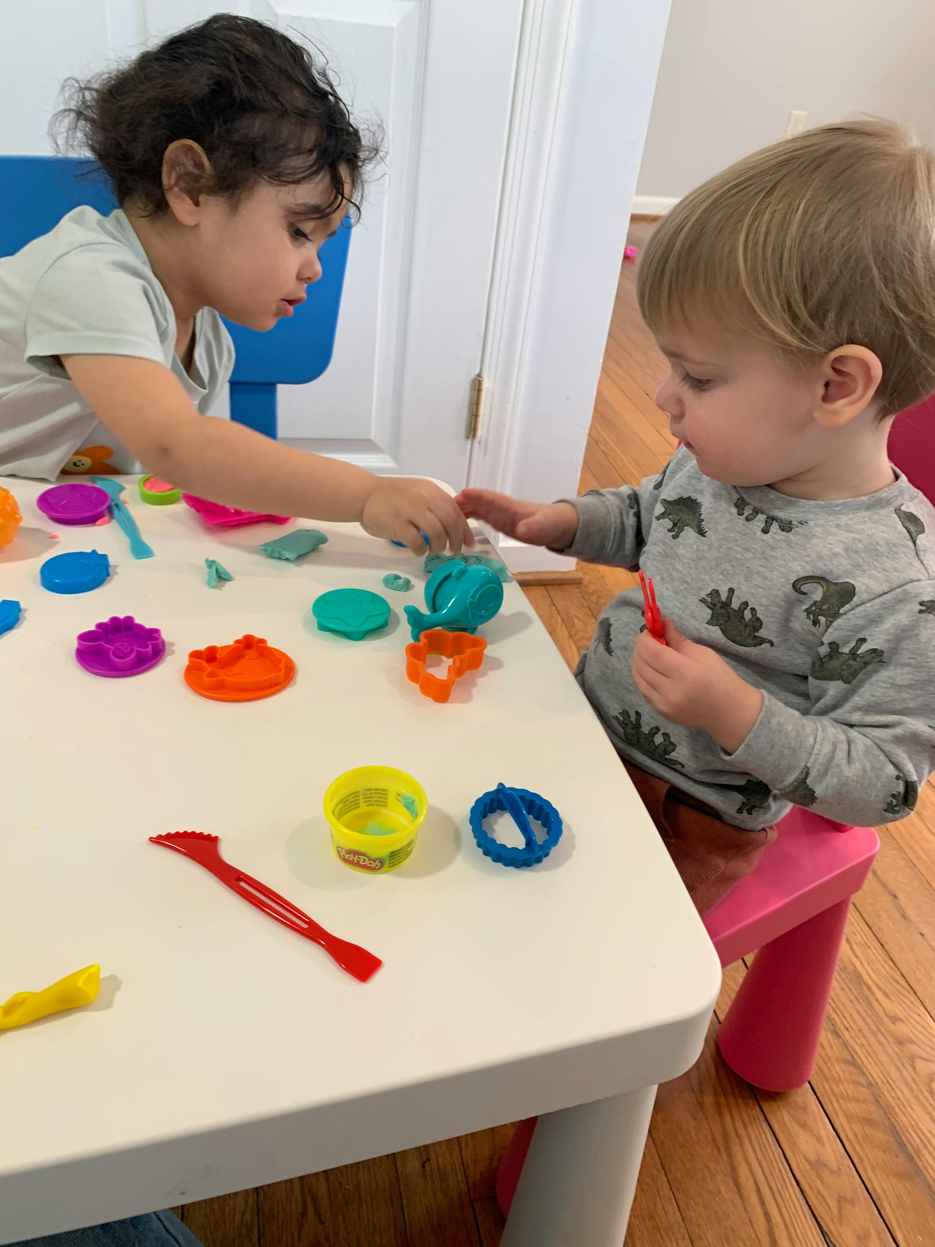 Two children playing with colorful playdough at a table