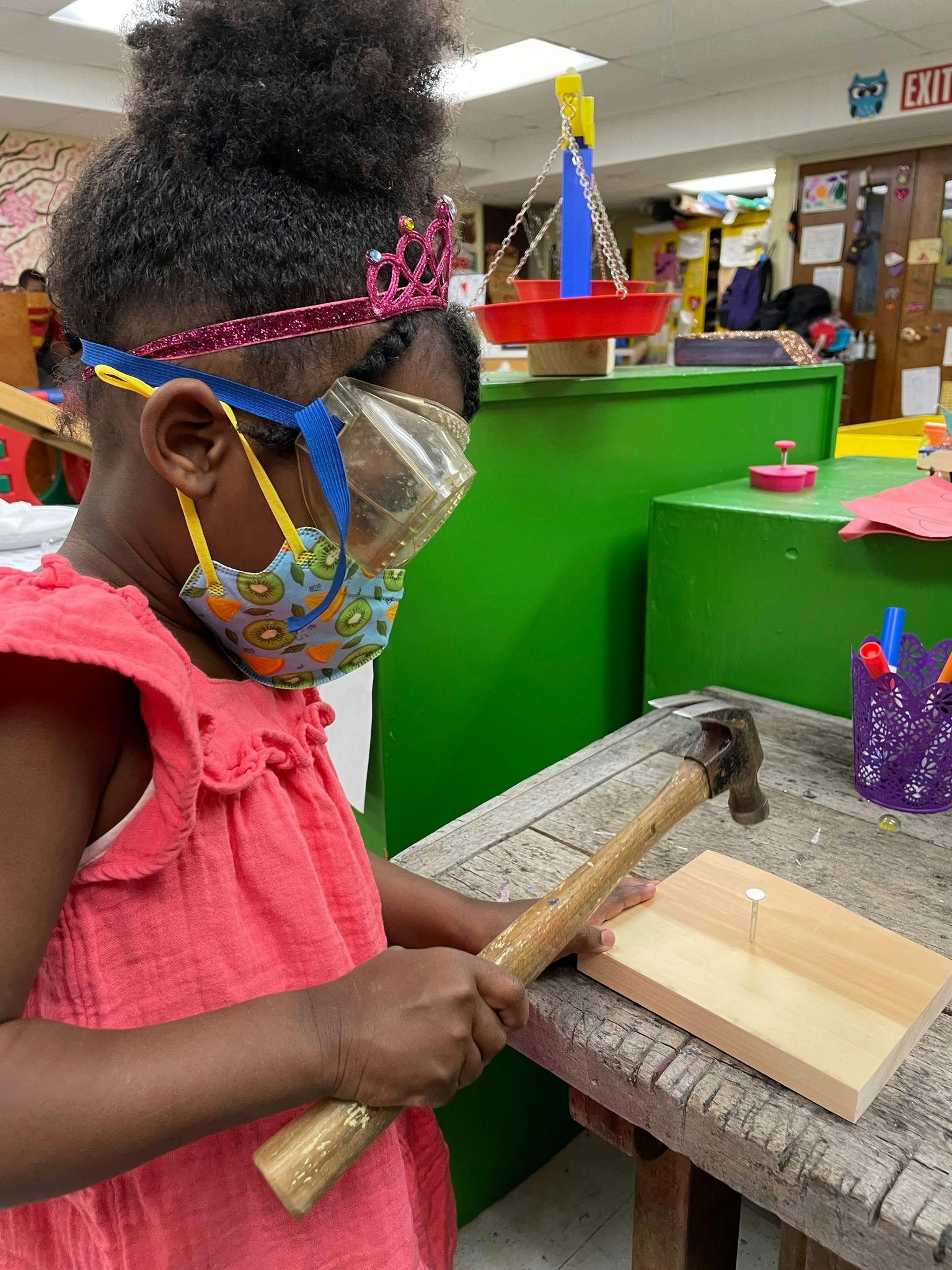 Child in safety goggles and mask hammering a nail into wood