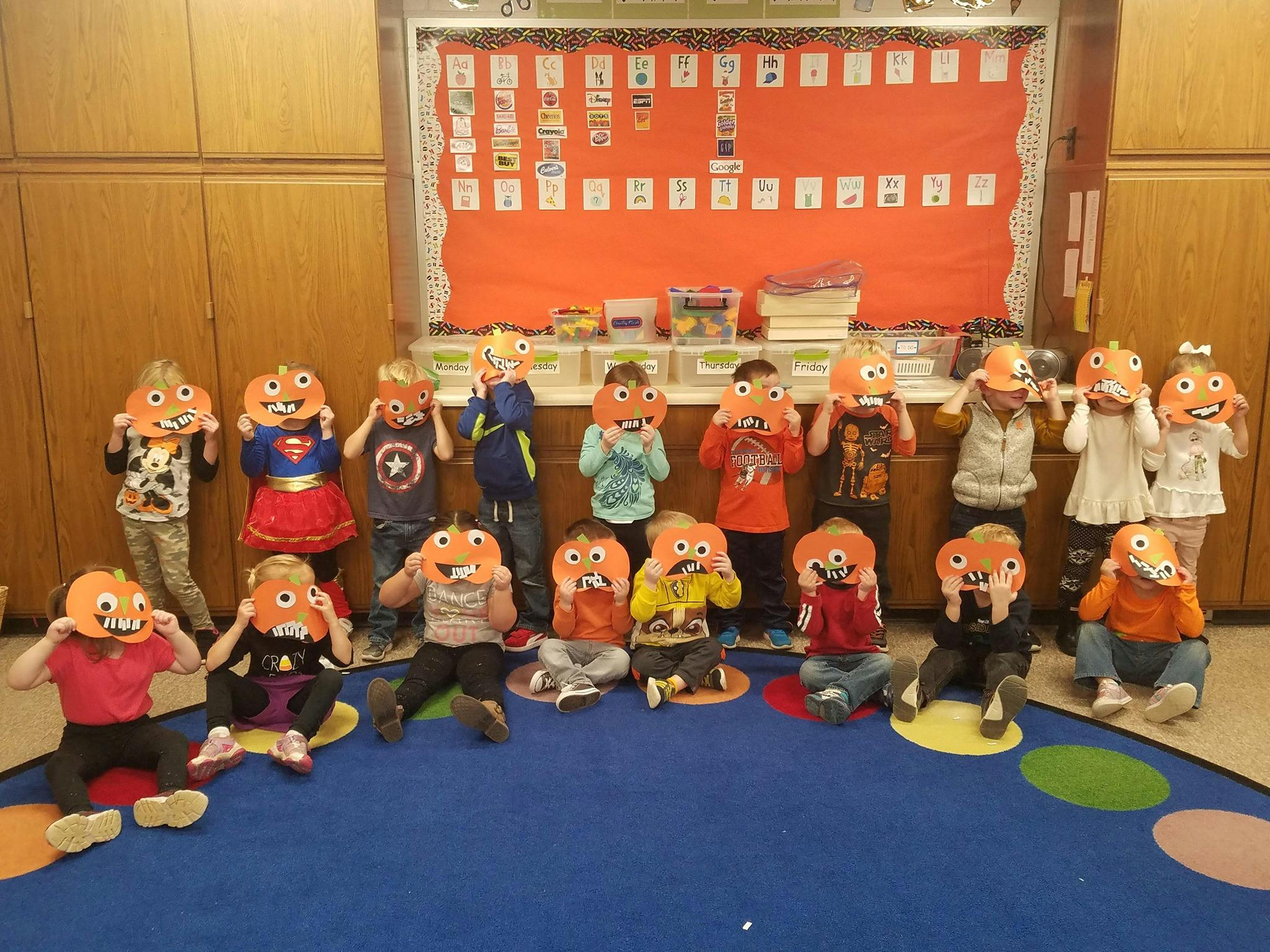 Group of children holding pumpkin masks over their faces in a classroom