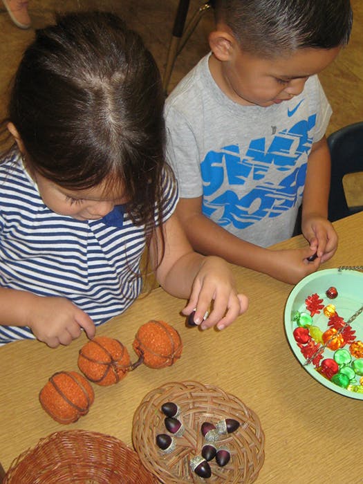Two children playing with small pumpkins and acorns