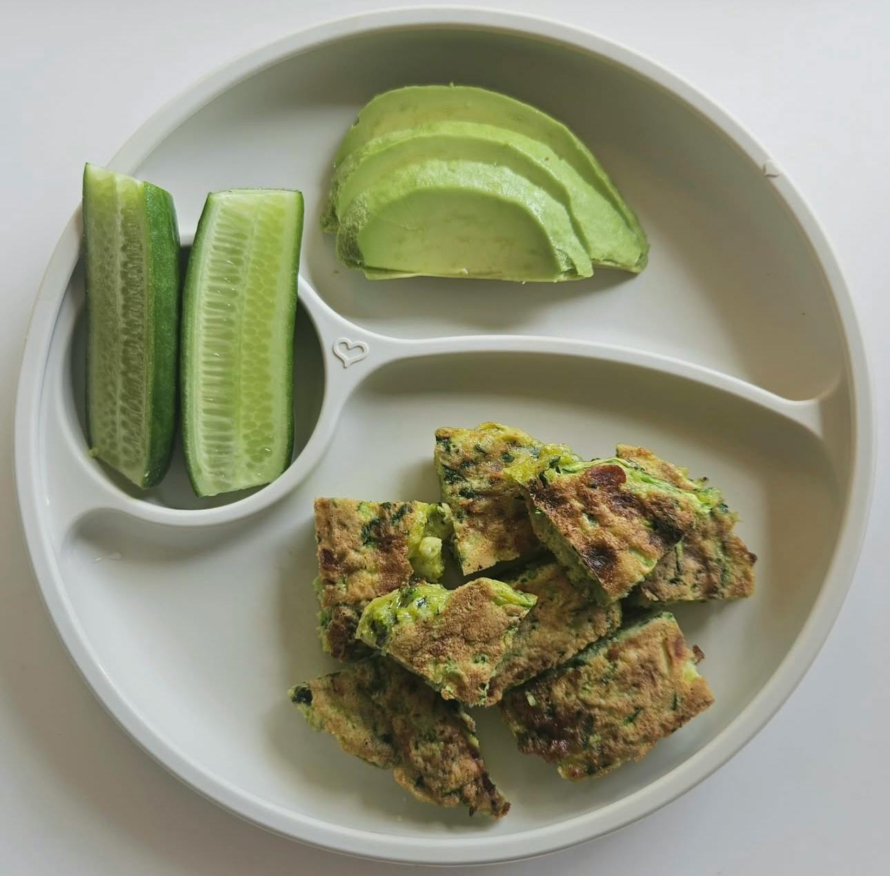 Divided plate with cucumber spears, sliced avocado, and baked squares