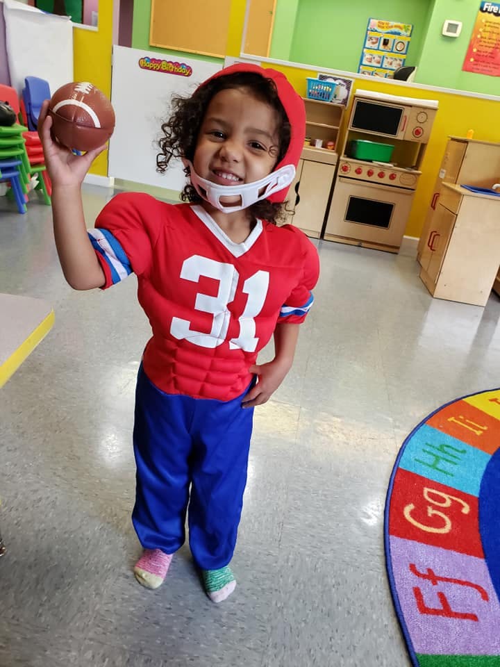 Child in football uniform holding a football in a classroom