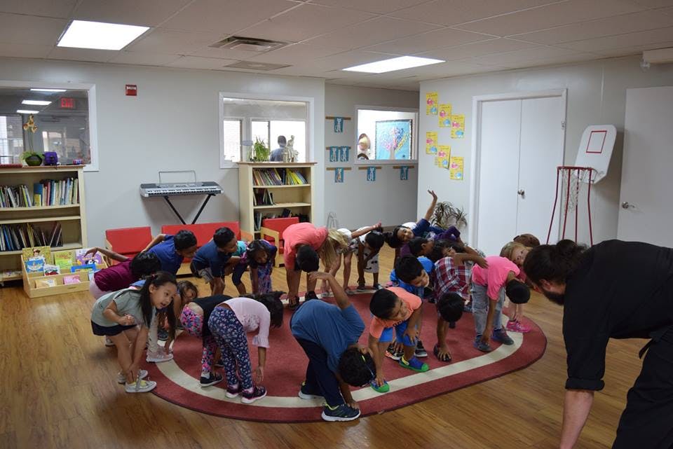 Group of children and adults bending over in a classroom