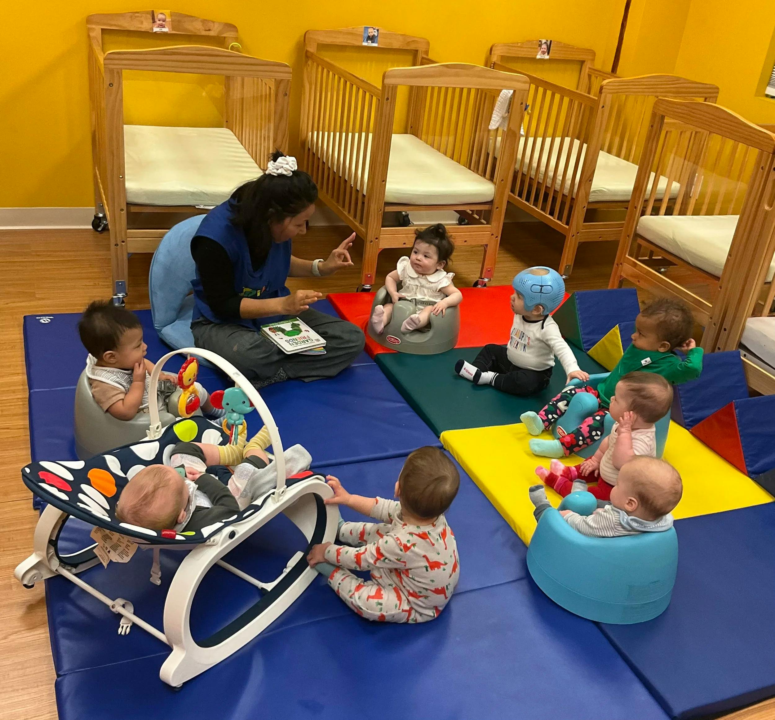 Person reading a book to seven babies in a daycare
