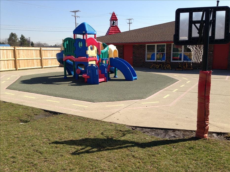Colorful playground structure on soft ground, next to a basketball hoop