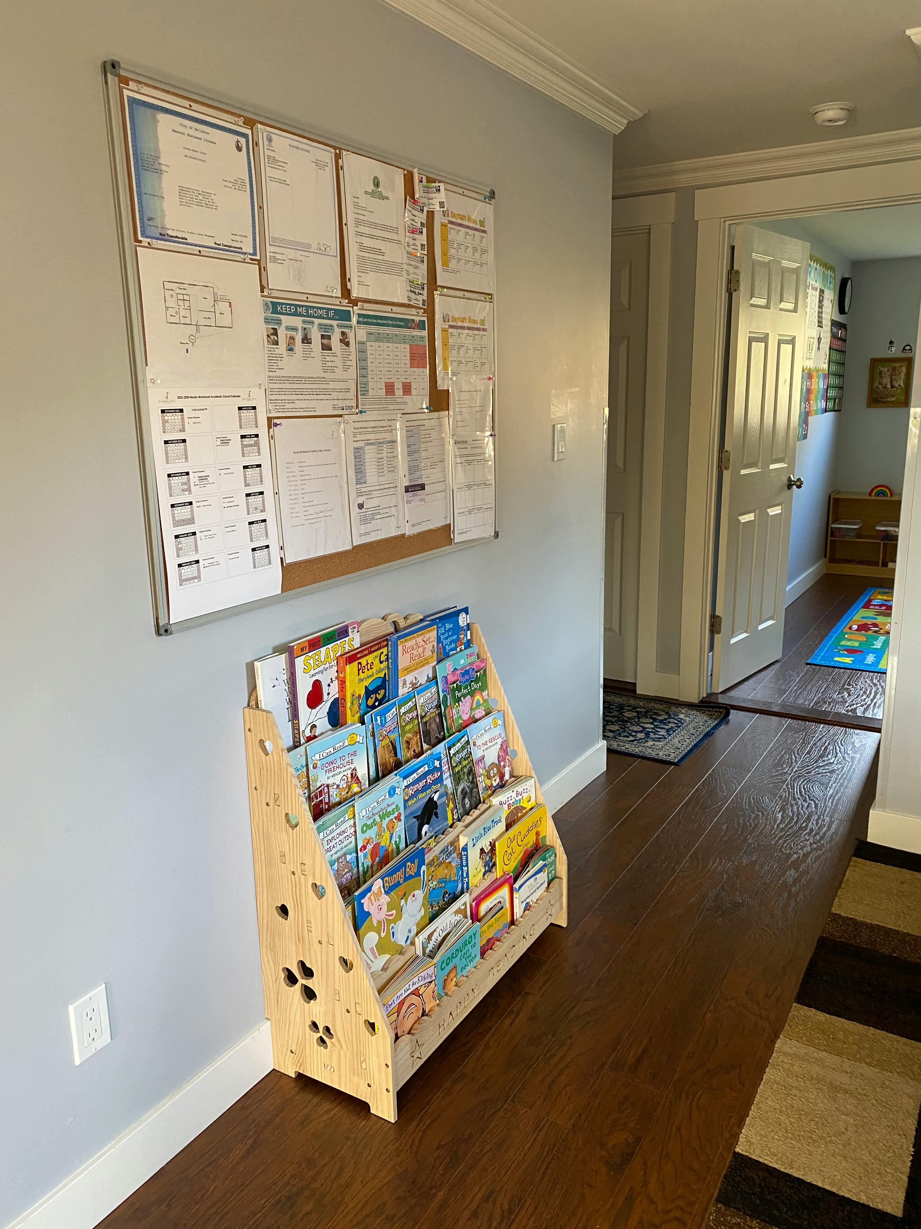 Bulletin board with papers and a wooden bookshelf filled with children's books