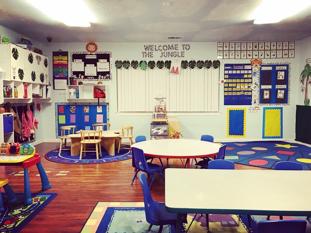 Preschool classroom with small tables and chairs, colorful rugs, and wall decorations