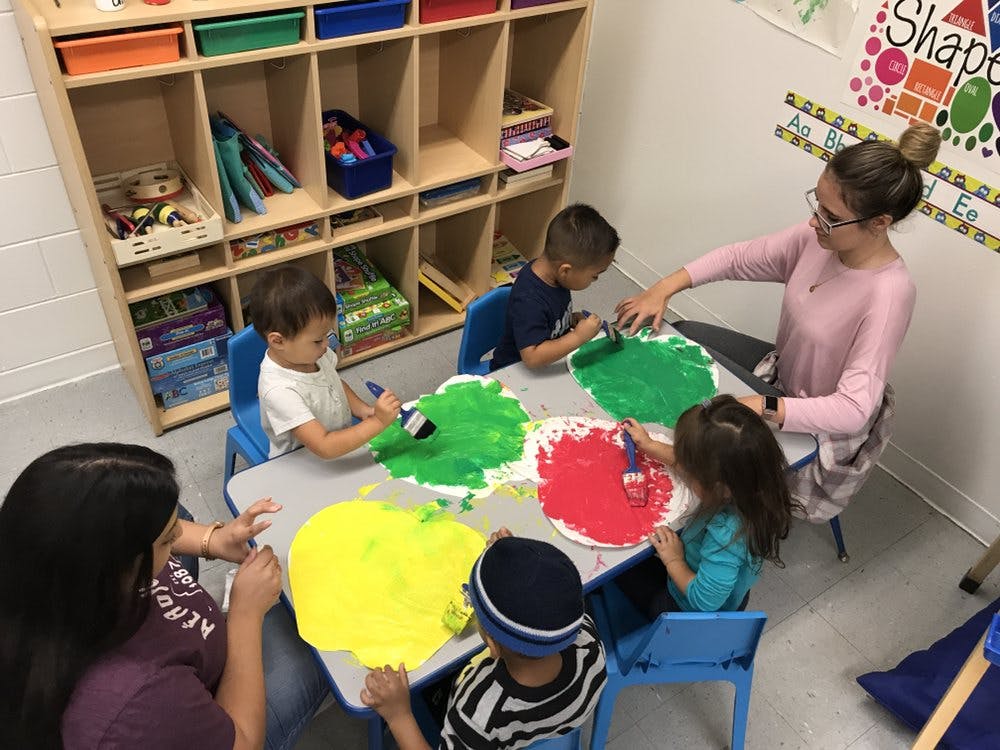 Adults and children painting at a table in a classroom