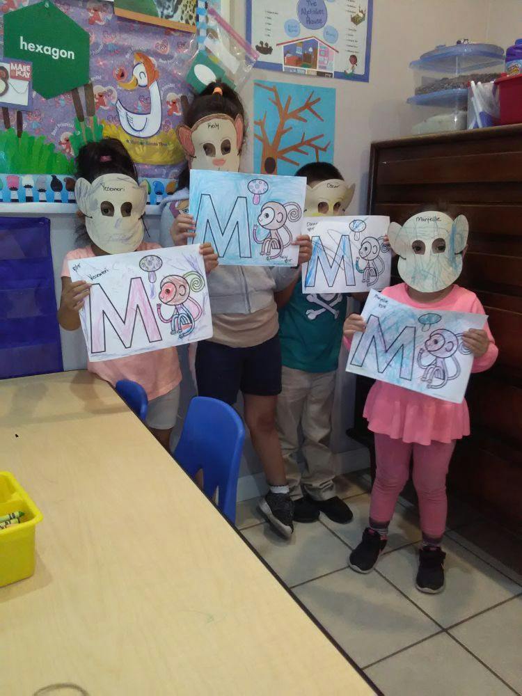 Children wearing masks holding up drawings of the letter M and a monkey