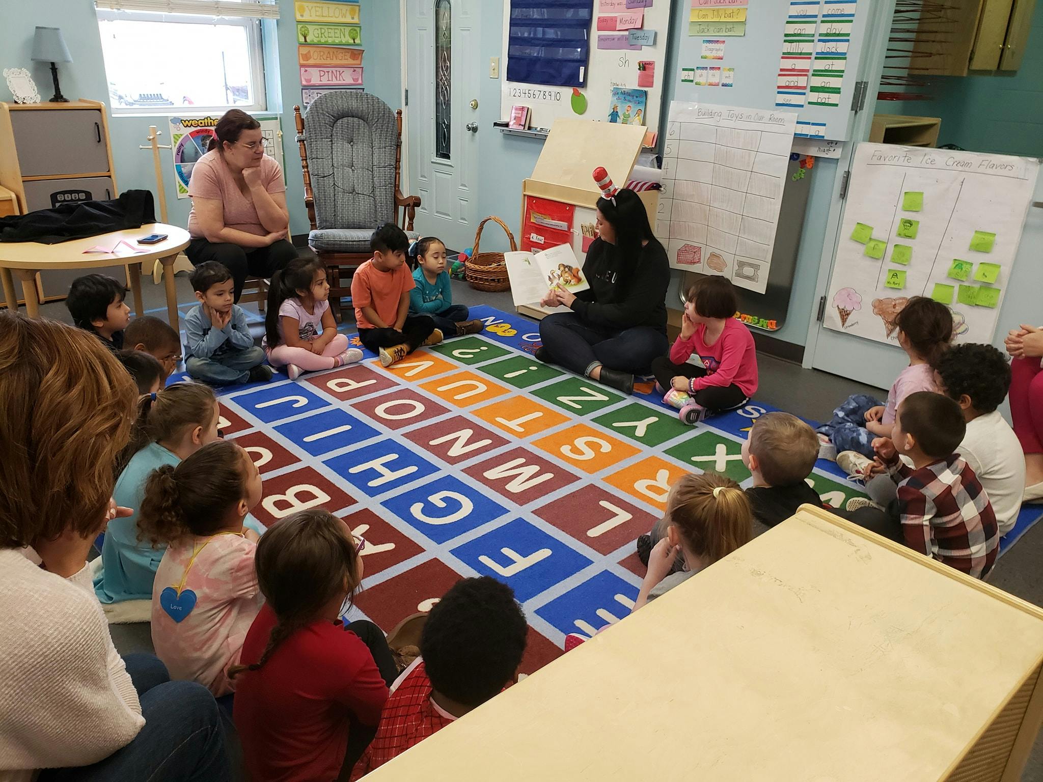 Adult reading a book to a group of children sitting on an alphabet rug